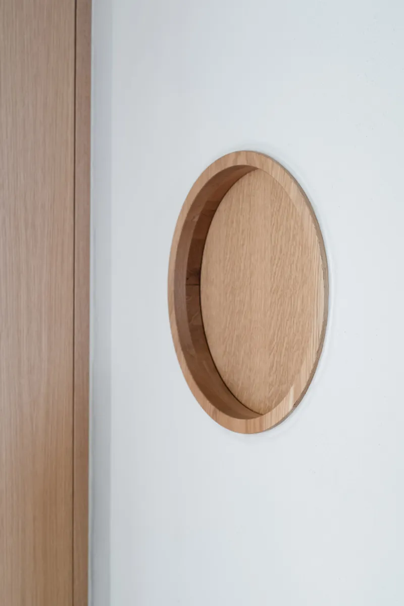 Recessed oak pocket door pull set flush into white plaster wall next to vertical wood panels