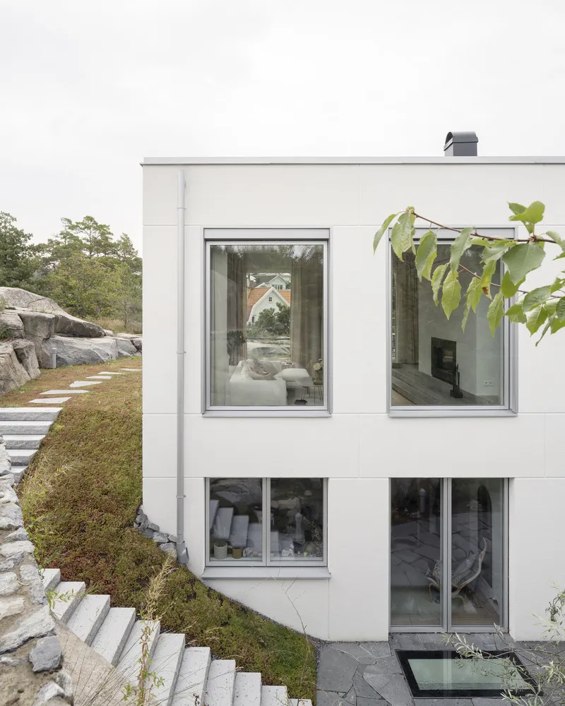 Exterior white facade with stacked windows opening onto moss-covered slope and granite stone steps
