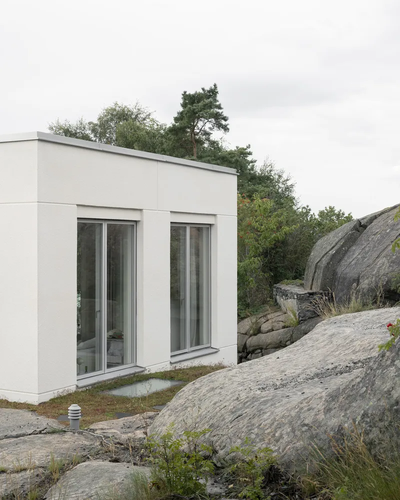 White facade with two glazed doors emerging from natural granite outcrop and low vegetation