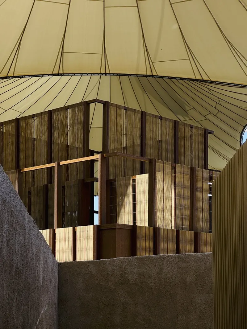 Interior view of layered timber screens beneath a pleated fabric ceiling with warm afternoon light