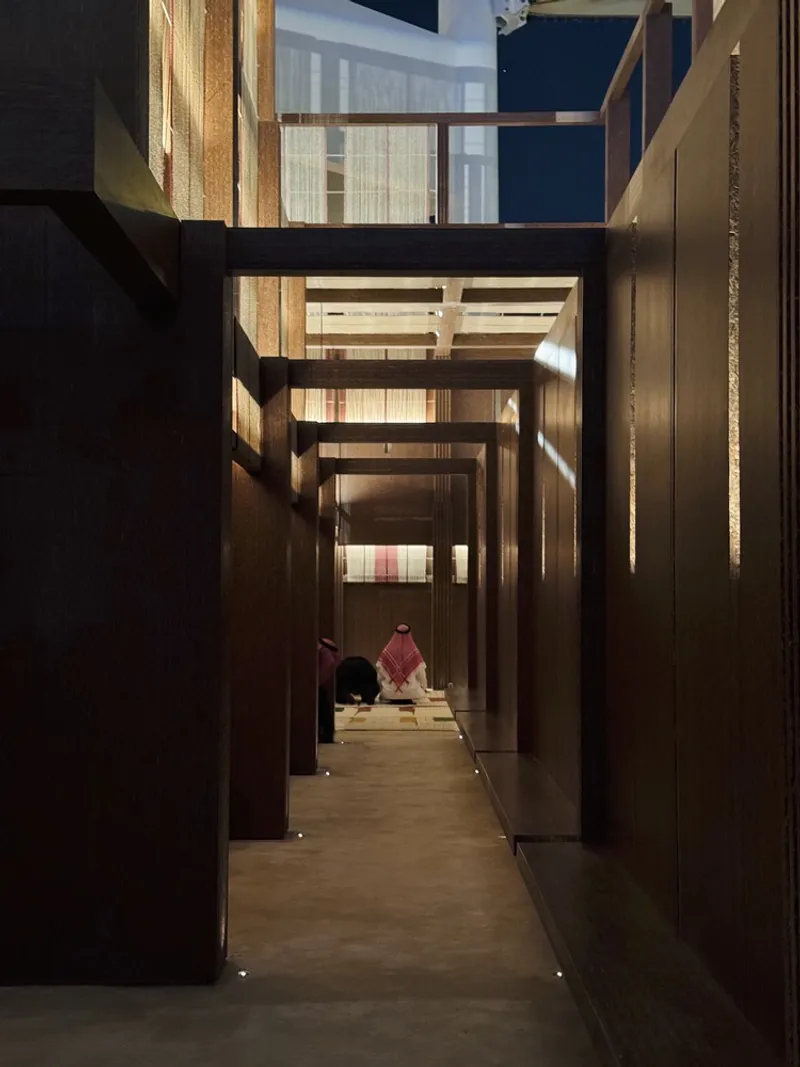 Interior corridor with dark timber walls and overhead bridges lit by recessed floor lighting at dusk
