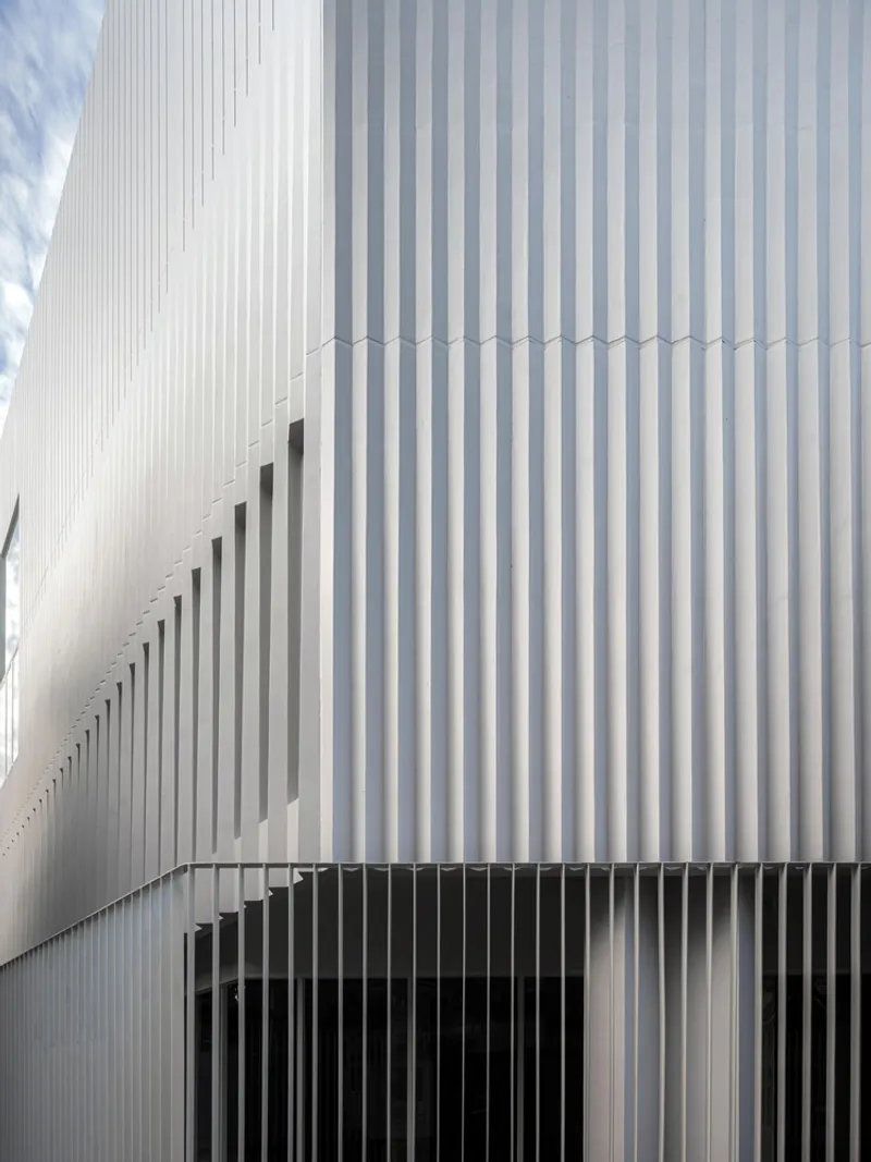 Detail of the white corrugated metal facade with vertical slot openings and dark horizontal base screening