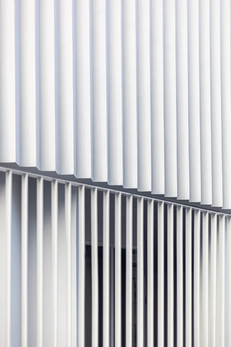 Close-up of white vertical metal fins meeting at a diagonal seam in soft daylight