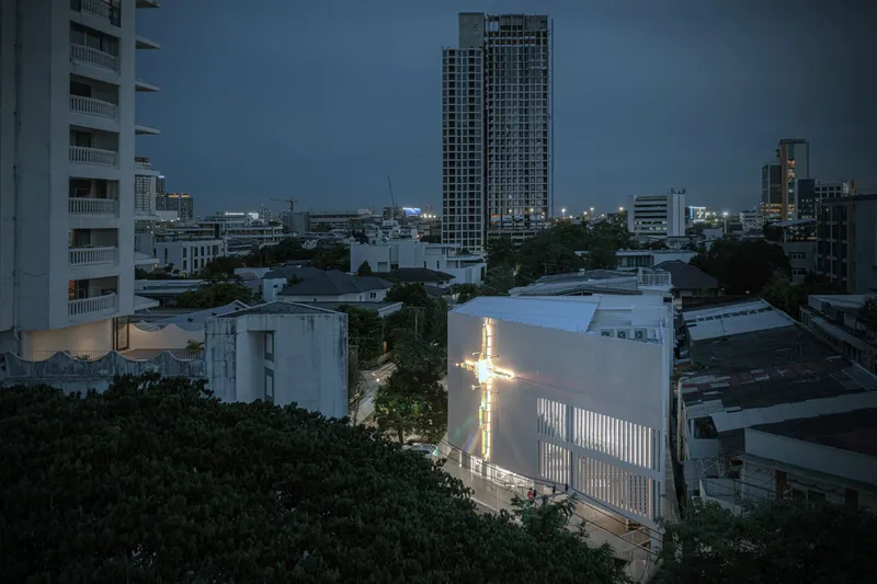 Elevated view of the illuminated cross on the corrugated facade at dusk among surrounding buildings
