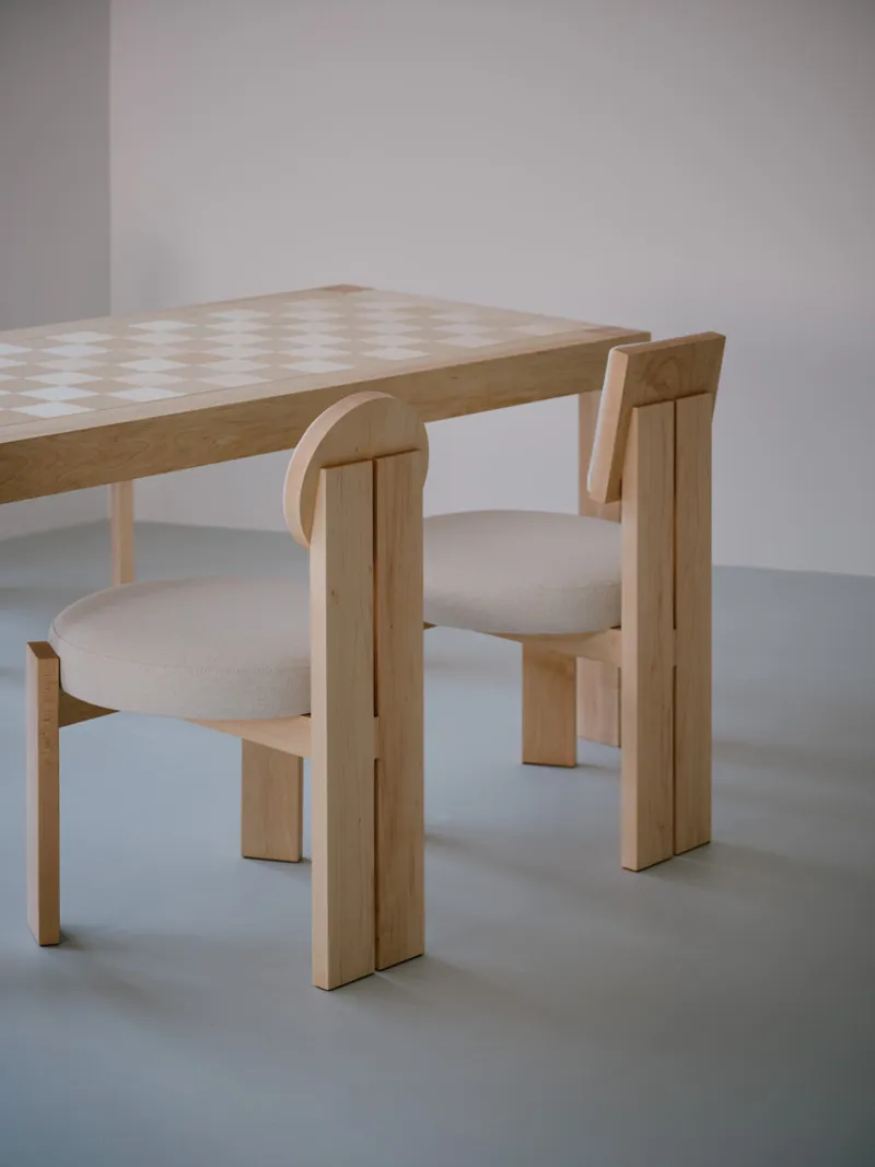 Close-up of checkerboard-patterned timber tabletop with two upholstered chairs on grey polished floor