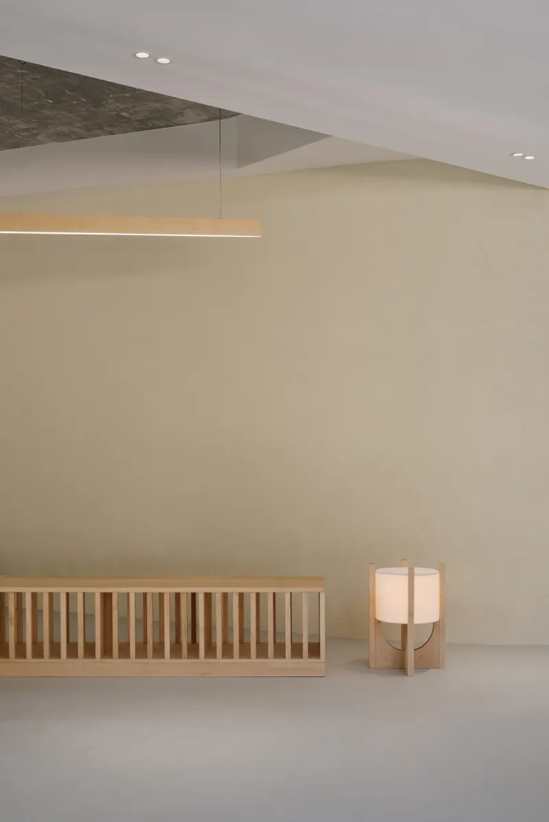 Interior corner with curved cream wall, suspended linear light fixture, and timber lantern on polished floor