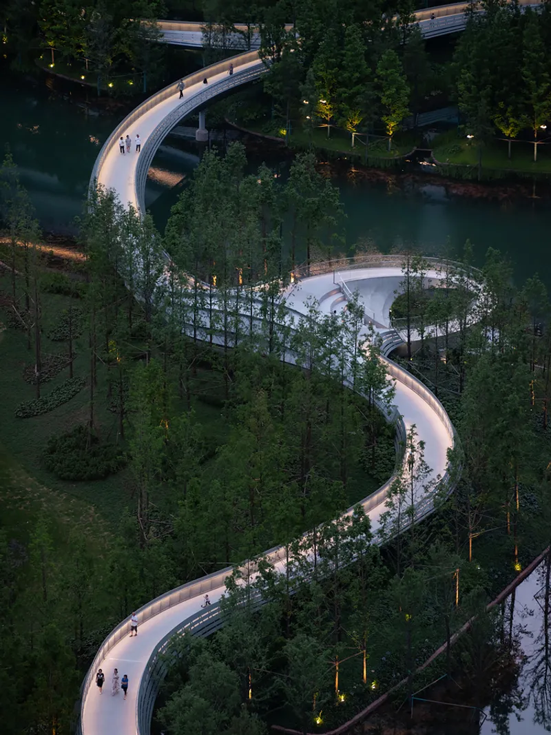 Winding illuminated concrete pathway through the forested wetland with visitors at dusk
