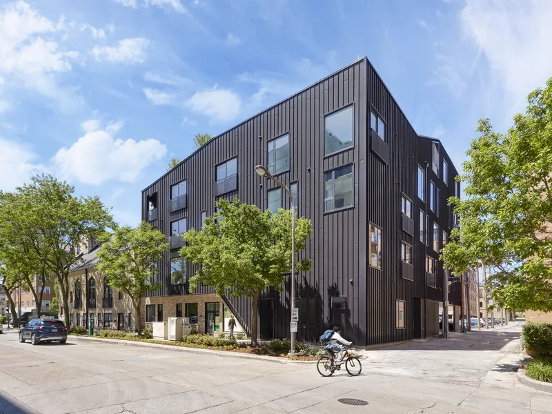 Corner view of the dark vertically ribbed cladding with scattered punched windows and a cyclist on the street