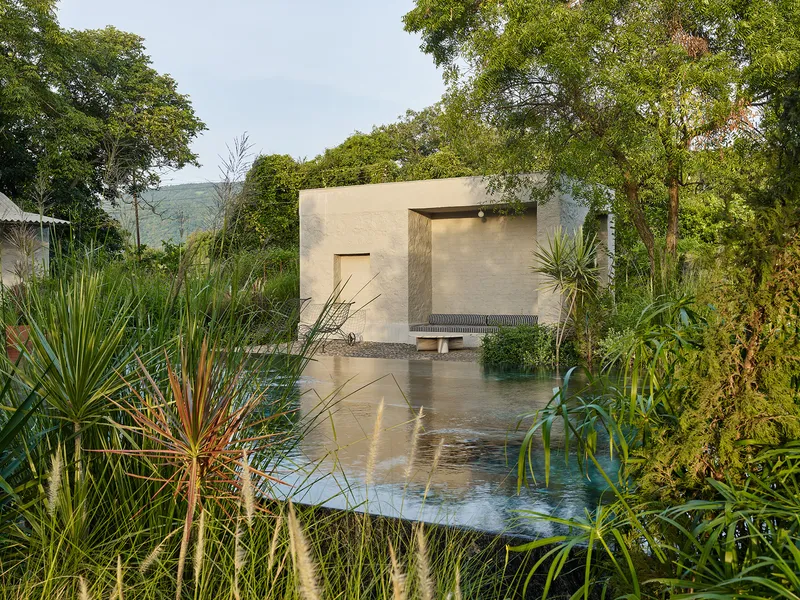 Pavilion with rendered walls and shallow water pool surrounded by native grasses and trees