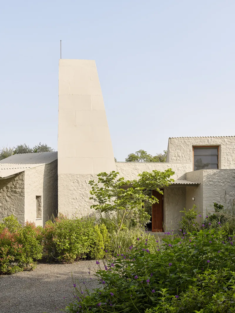 Entry facade with tapered tower and timber door set within planted garden beds under cloudy skies