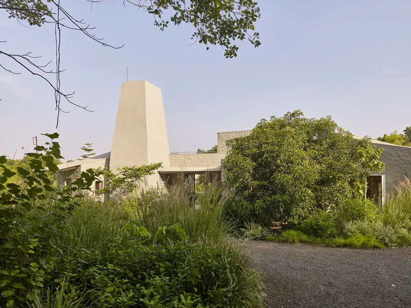 Approach through gravel drive with tall grasses framing the chimney tower and corrugated roof forms