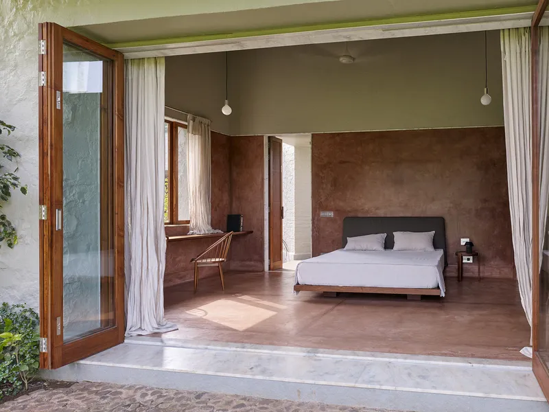 Bedroom with open timber-framed doors revealing terracotta-washed walls and polished concrete floor in afternoon light