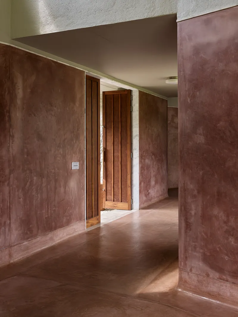 Interior hallway with terracotta plaster walls and timber door framing view through successive rooms