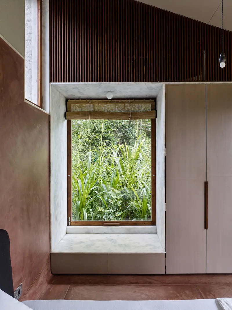 Deep window recess with concrete frame overlooking planted garden bed with tall grasses