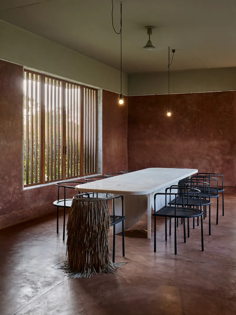Dining room with pendant bulbs and vertical timber screen filtering daylight beside terracotta plaster wall