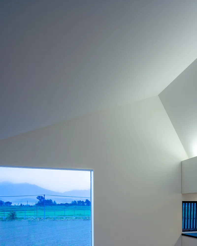 Angled ceiling planes meeting above a picture window overlooking farmland at twilight