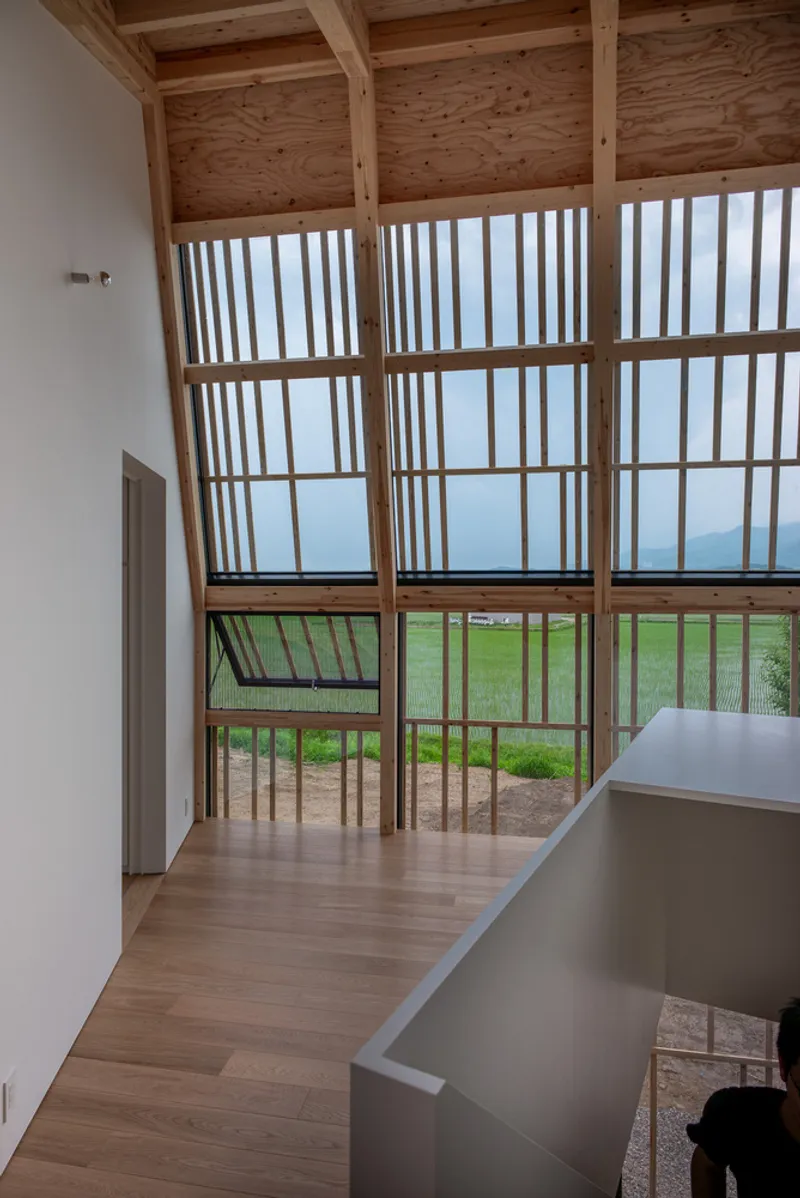 Double-height timber screen wall with vertical slats framing a view of green fields