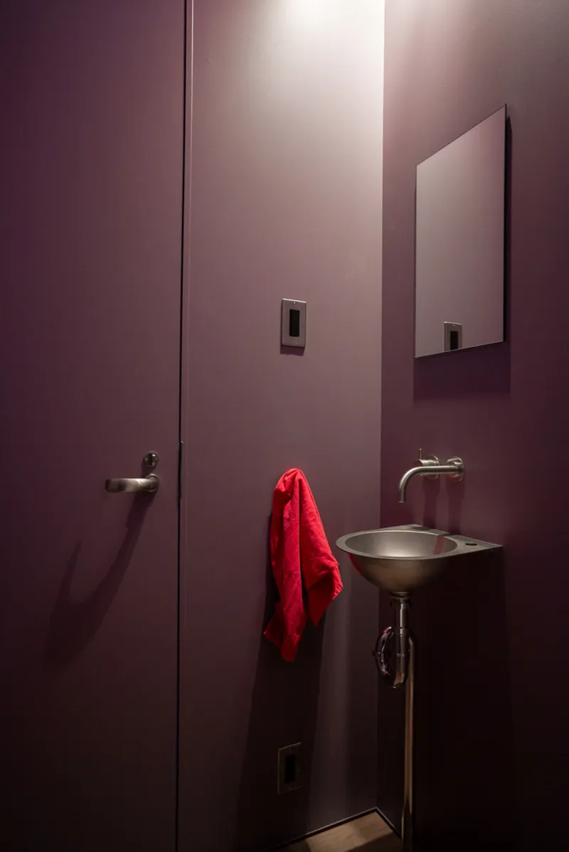 Purple bathroom with pedestal sink, red towel, and concealed door under soft lighting
