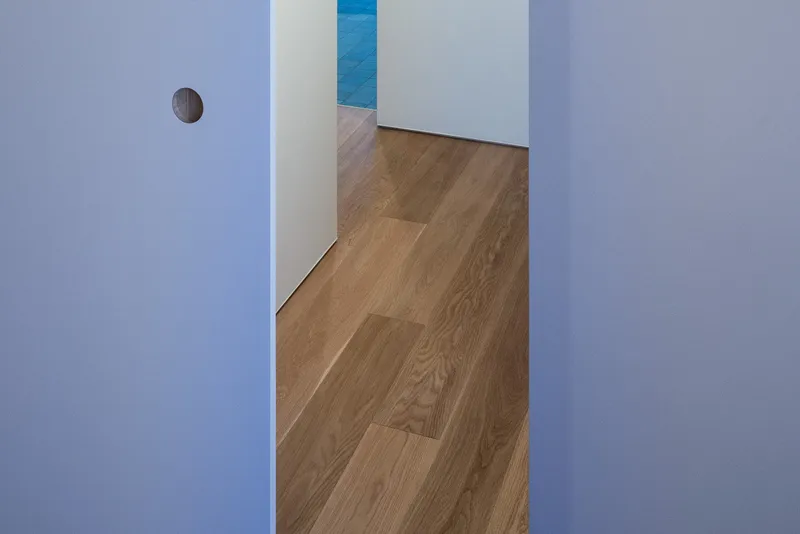 White corridor with timber flooring leading through doorways to a blue accent wall