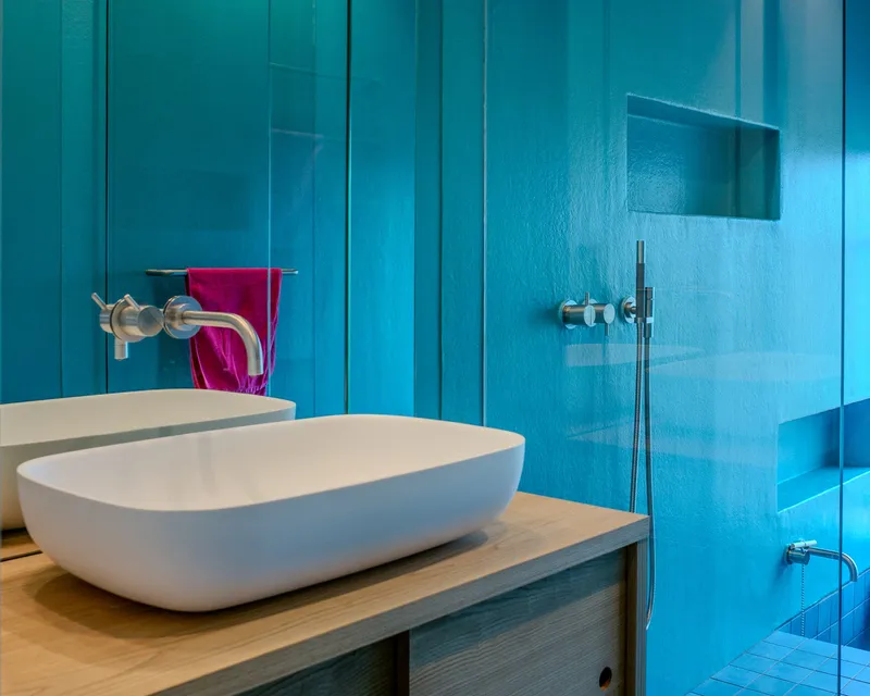 White oval basin on timber counter against turquoise tile walls with glass shower partition