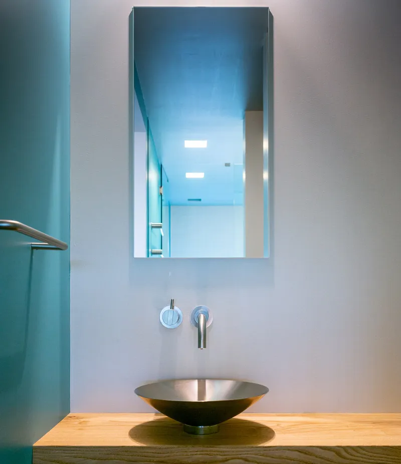 Conical metal vessel sink on timber vanity beneath a recessed mirror and wall-mounted faucet