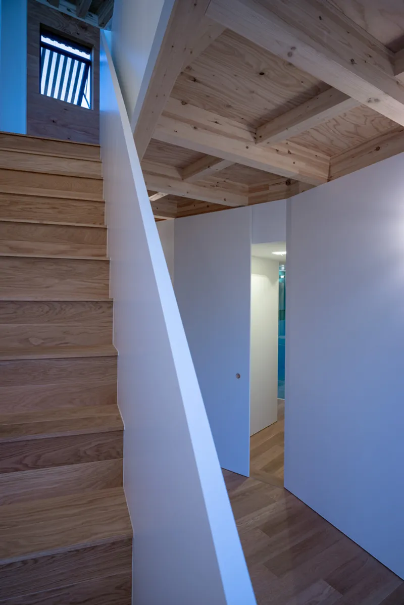 Timber staircase rising past white walls and exposed wood beam ceiling with concealed doorway