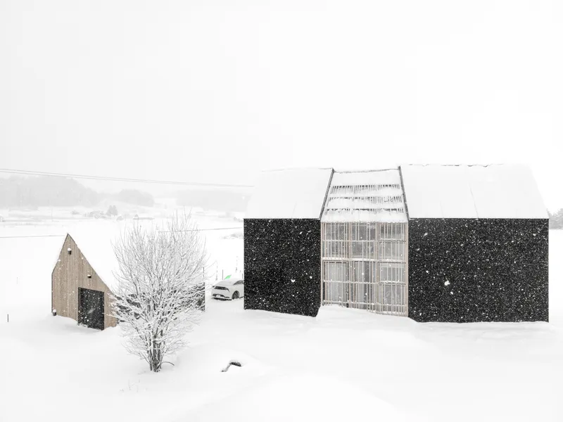 Courtyard view showing the glazed volume and black panel facade during snowfall