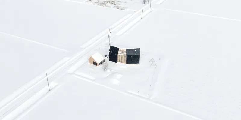 Drone perspective of the timber and black-clad volumes surrounded by snow and utility poles