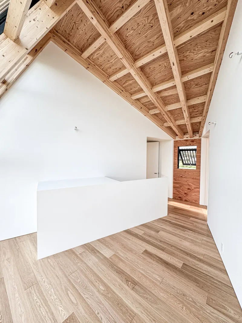 Upper-level hallway with exposed timber roof rafters, white walls and oak flooring leading to a window