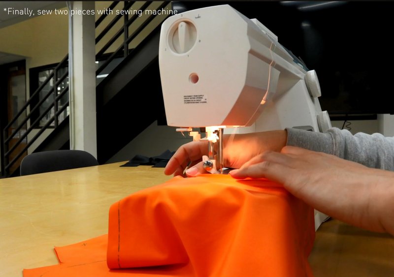Sewing machine stitching orange fabric components together under indoor workshop lighting