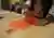 The image shows a person fixing two pieces of orange fabric together using liquid stitch. The fabric