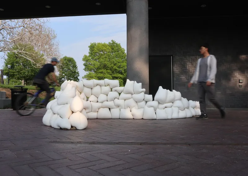 Cyclist and pedestrian passing white inflatable seating beneath covered pavilion with concrete column