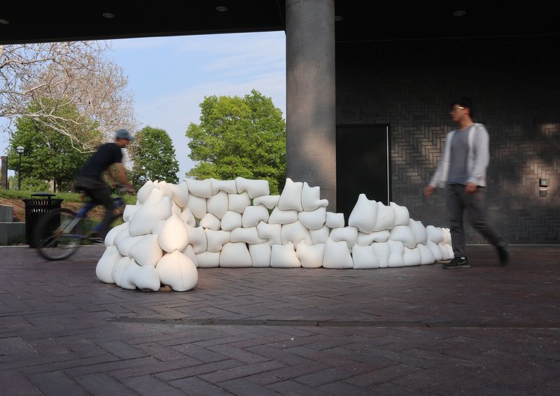 Cyclist and pedestrian passing white inflatable seating beneath covered pavilion with concrete column