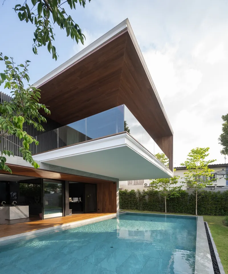 Cantilevered timber-clad upper volume over the swimming pool with glass balustrade and young trees