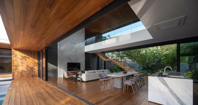 Open-plan living area with timber ceiling, concrete wall, floating staircase and garden view through glass doors