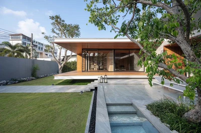 Garden view showing the timber-clad pavilion with glass walls and overhanging roof beside a narrow lap pool