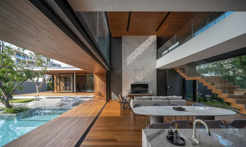 Open-plan interior with timber ceiling, concrete fireplace wall, and double-height space visible beyond the kitchen