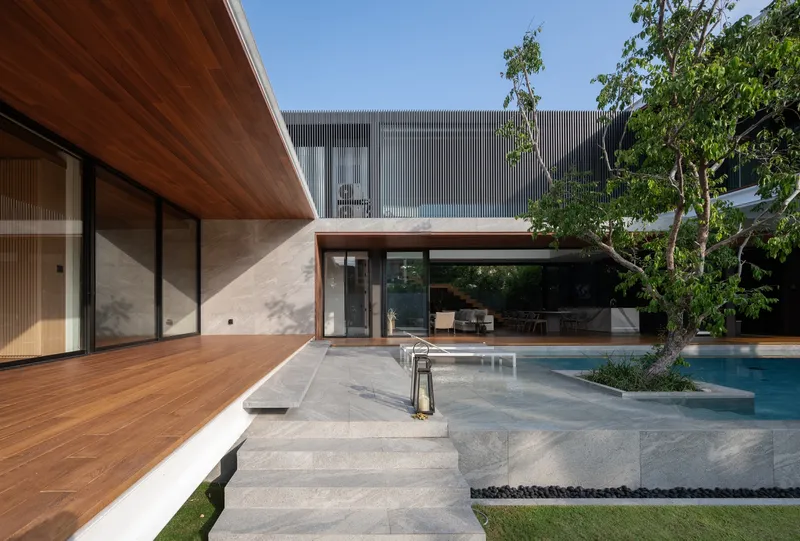 Courtyard view with timber deck, concrete pool edge, and corrugated metal-clad upper volume under trees