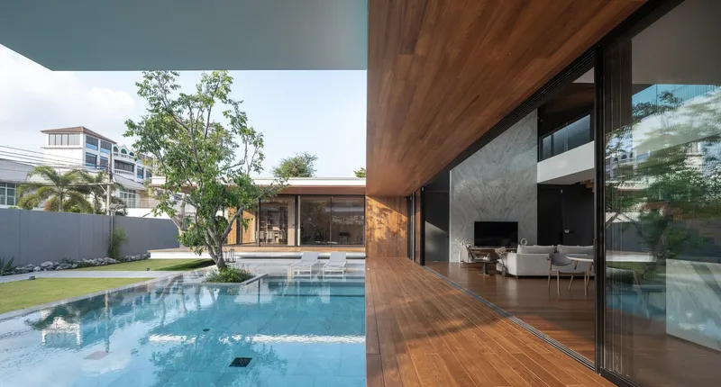 View across swimming pool toward glazed pavilion and timber-clad upper volume with planted courtyard tree