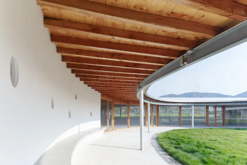Covered walkway with exposed timber beams and white walls curving around a grassed courtyard