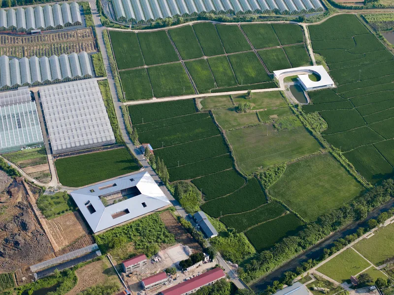 Aerial view of a rectangular white roof with central courtyard surrounded by green agricultural fields
