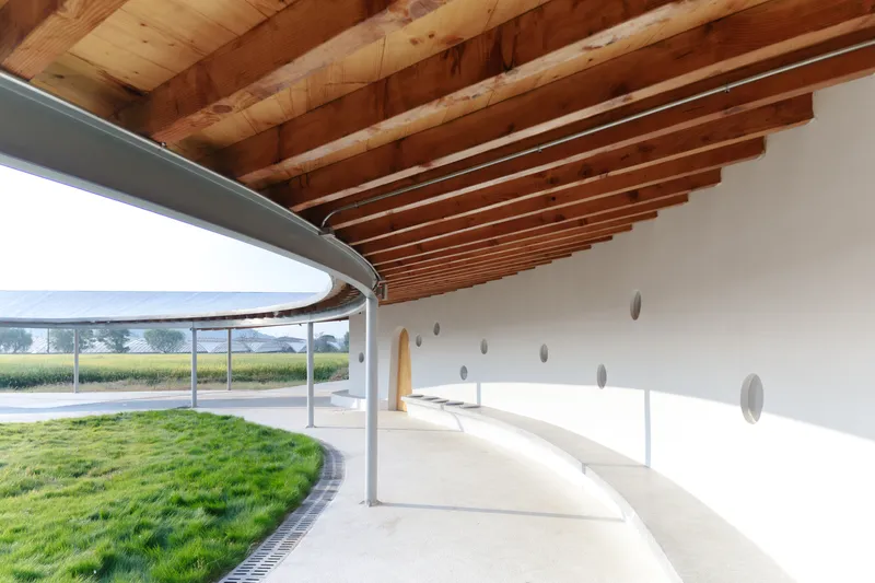 Covered walkway with exposed timber beams curving around a circular planted courtyard in morning light