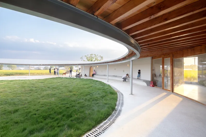 Circular courtyard with grass lawn and drainage channel under a curved timber ceiling at sunset