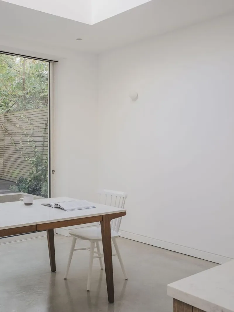 Corner window framing timber fence and greenery beside a walnut dining table