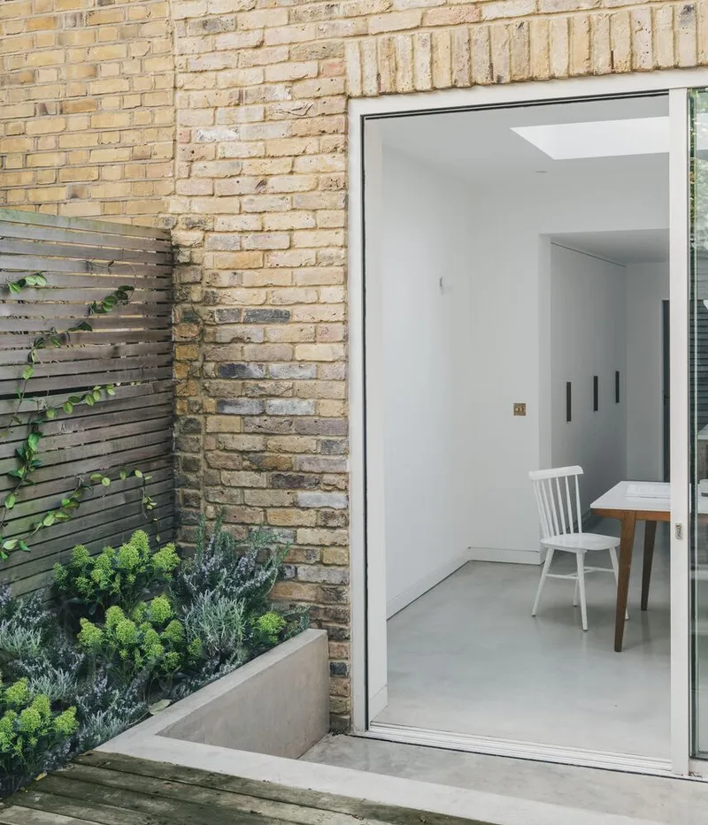 Courtyard threshold with planted bed against weathered yellow brick and horizontal timber slat screen