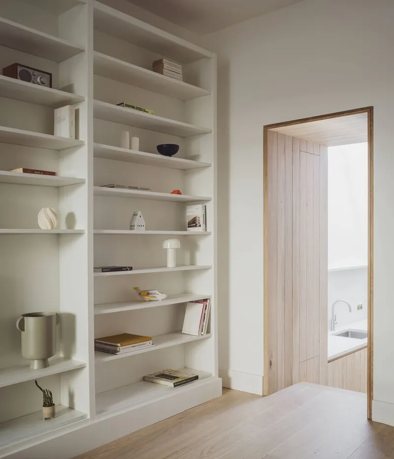 Built-in white shelving unit beside a timber-framed doorway with pale oak flooring