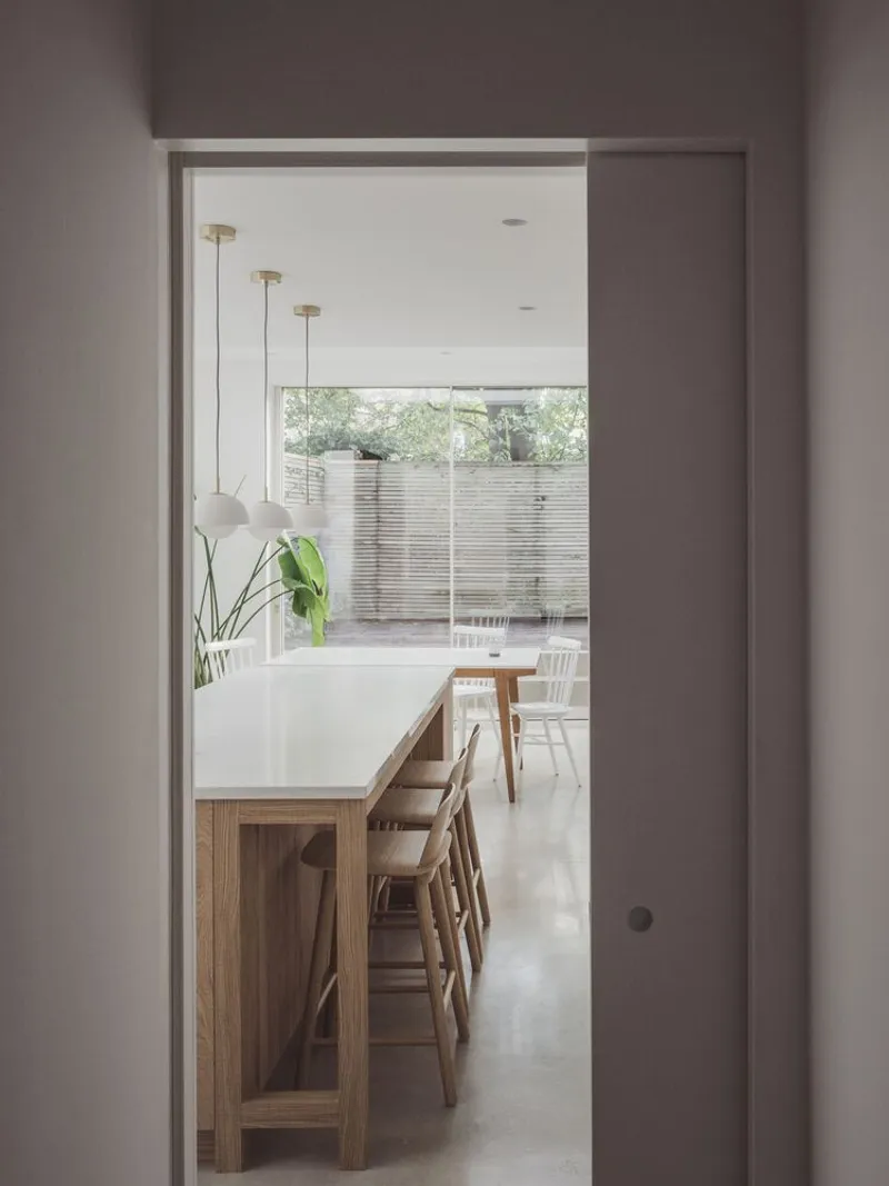 View through a doorway to a timber dining island with pendant lights and garden beyond