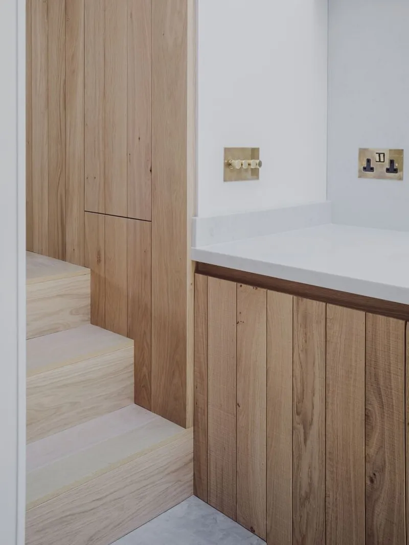 Junction of timber stair treads and oak cabinetry with brass electrical switches on white wall