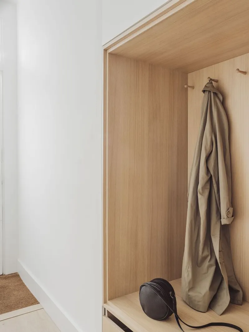 Timber-lined coat alcove with hanging garment and bag on cork flooring