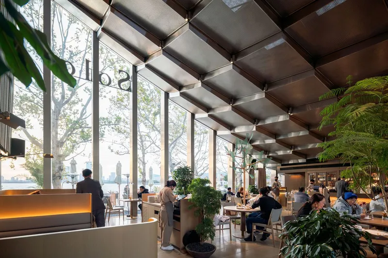 Interior dining hall with coffered ceiling panels, floor-to-ceiling windows overlooking bare winter trees and skyline